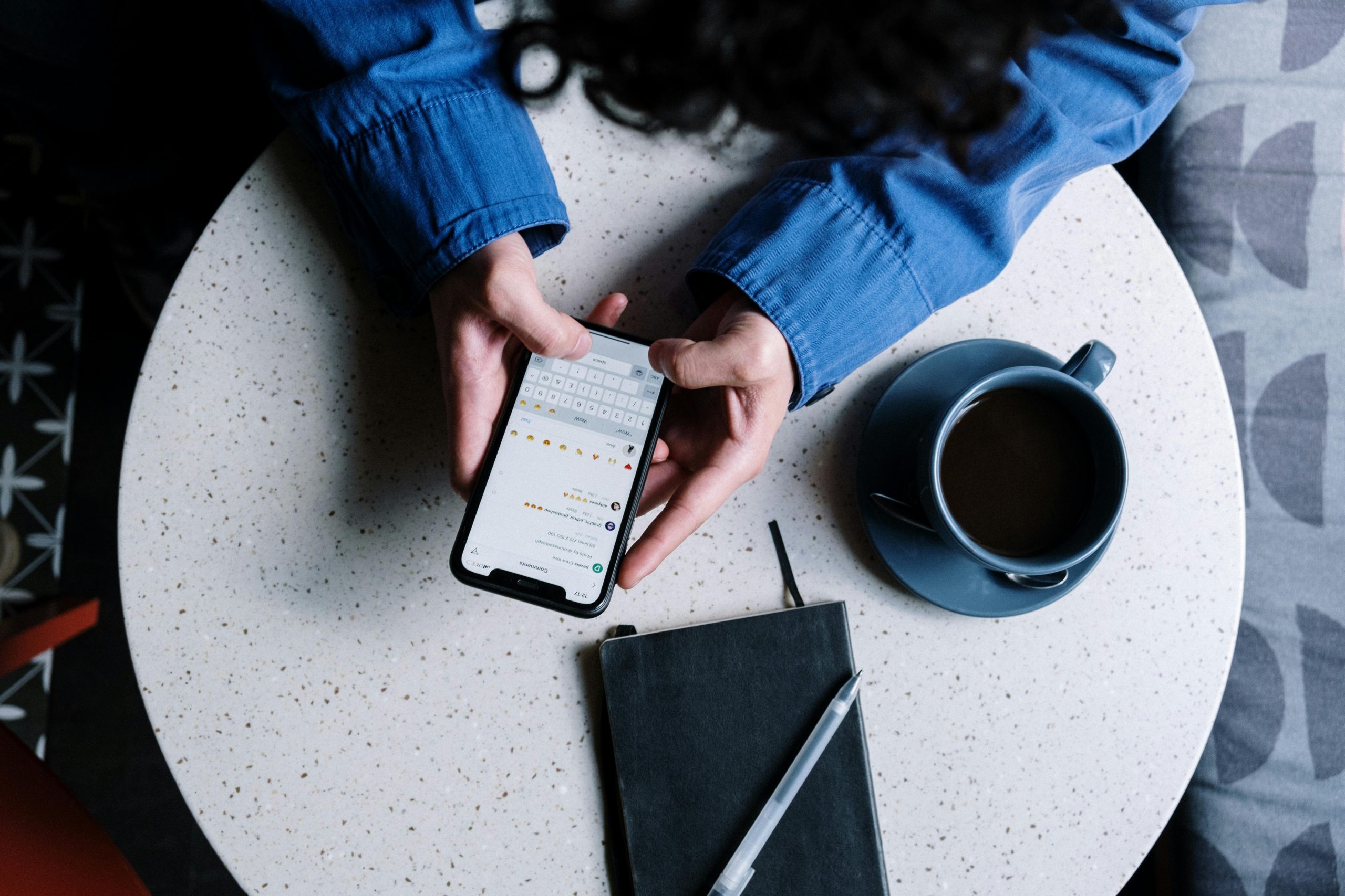 Person using smartphone at table with notebook and coffee, ideal for tech and lifestyle themes.
